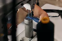 A close-up shows a person's hands guiding blue leather through a sewing machine to create PinkPantheress's custom ballet flats