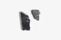 Two dark, jagged mineral pieces with white and red veins, possibly for Joe Burrow's chess set, lie on a white surface