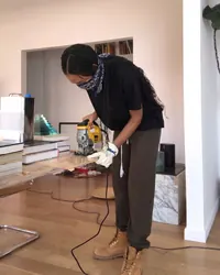 Solange Knowles, wearing a bandana and work boots, uses a jigsaw to cut wood for her unfinished architectural sculpture