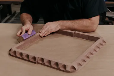 Joe Burrow sands a wooden frame with carved details, part of his custom chess set
